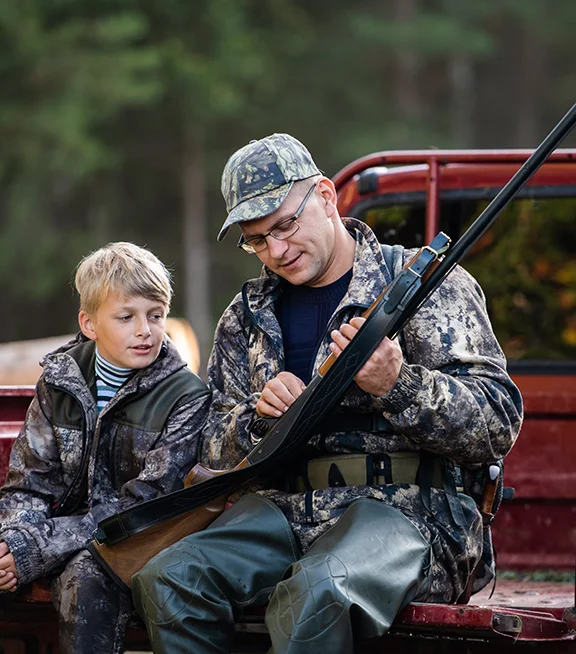 A father shows his son how to load a gun in the back of a pickup truck